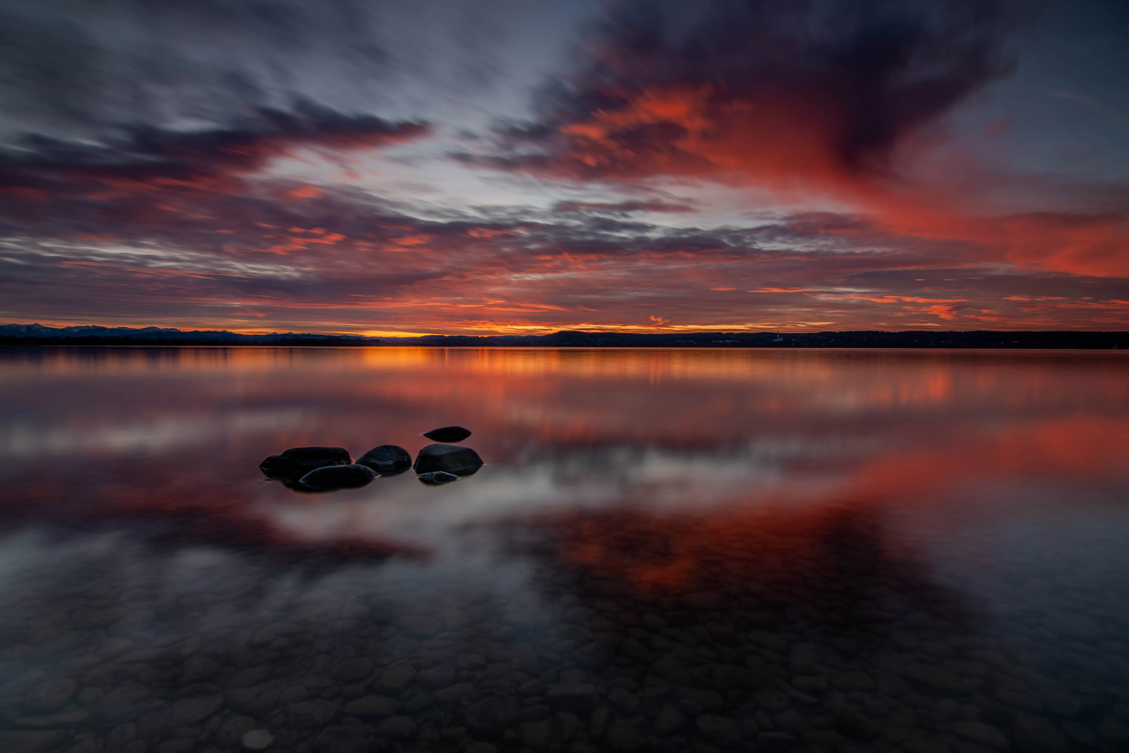 Abendrot über dem Ammersee, drei Steine liegen im spiegelglatten Wasser