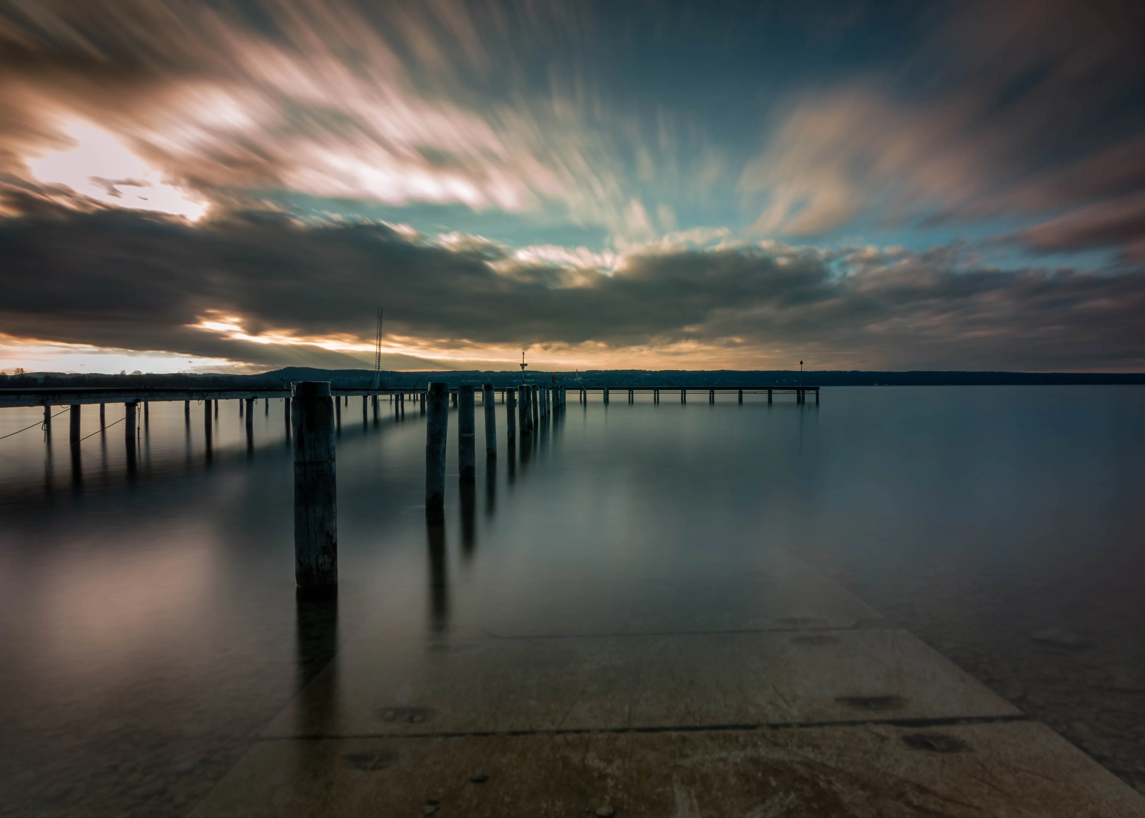 Holzpfähle im Ammersee am Abend, das Wasser liegt in Langzeitbelichtung glatt