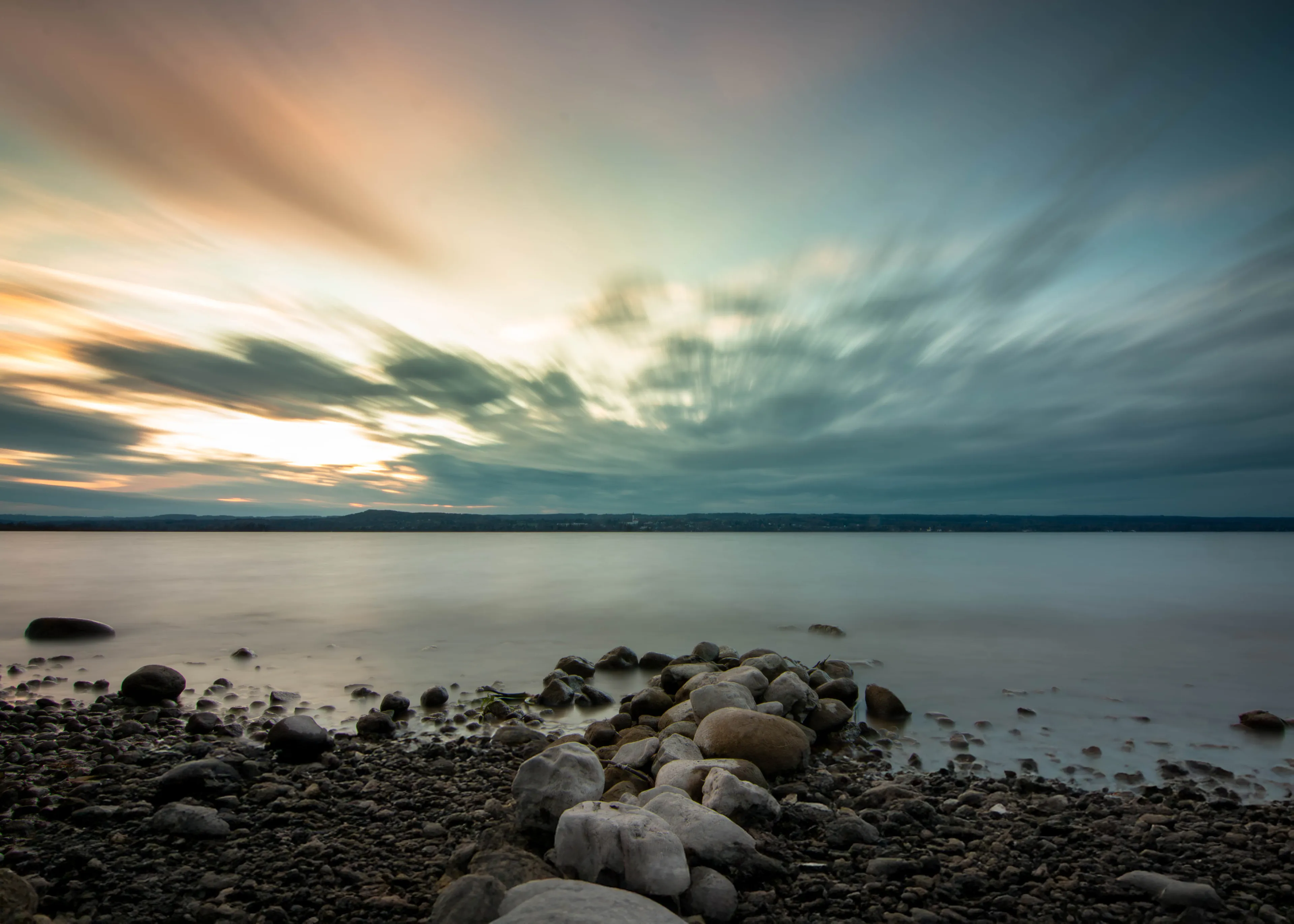 Runde Kiesel am Ufer des Ammersees, dahinter der weite Abendhimmel