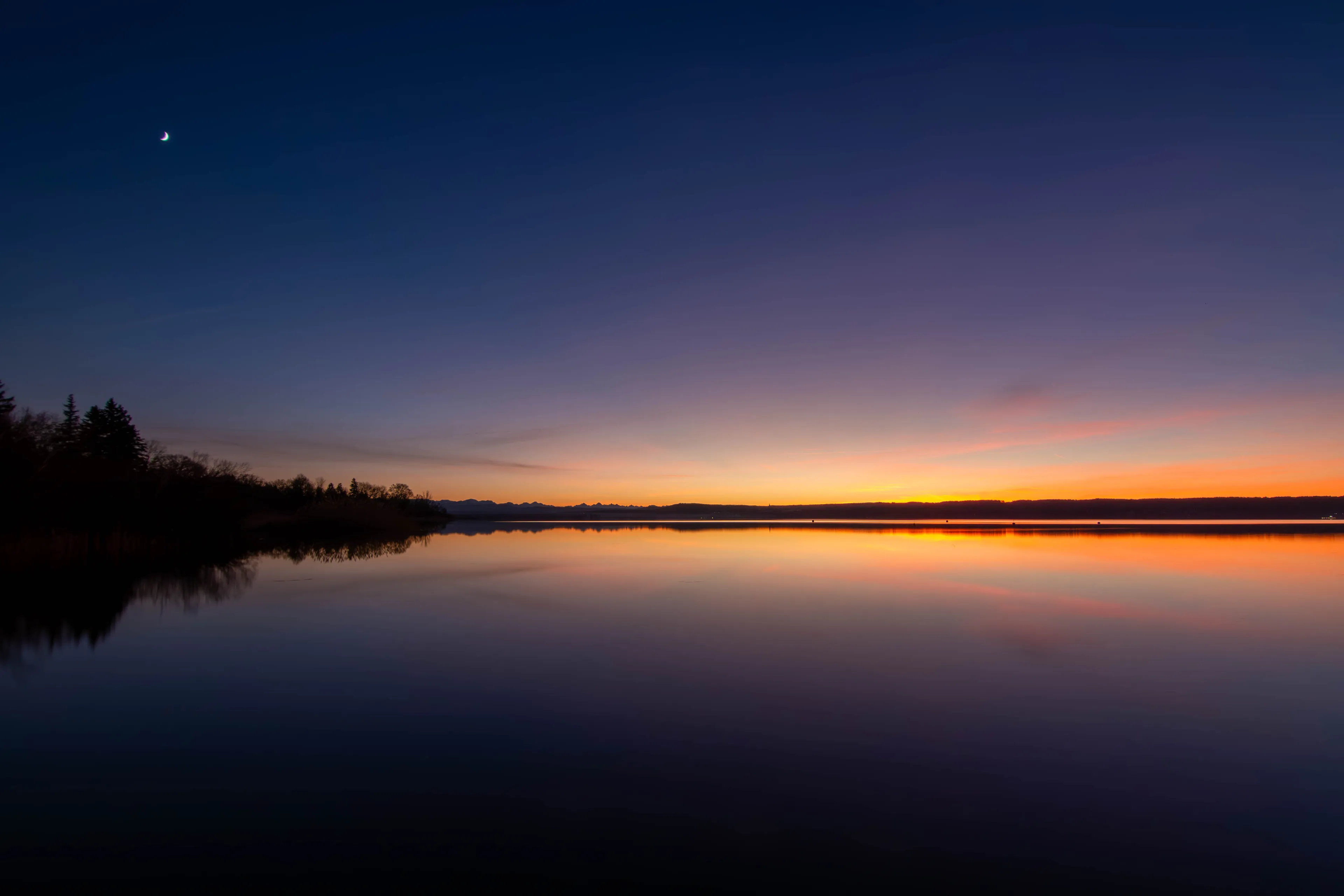 Das Ufer des Ammersees in der Dämmerung, der Himmel spiegelt sich im ruhigen Wasser