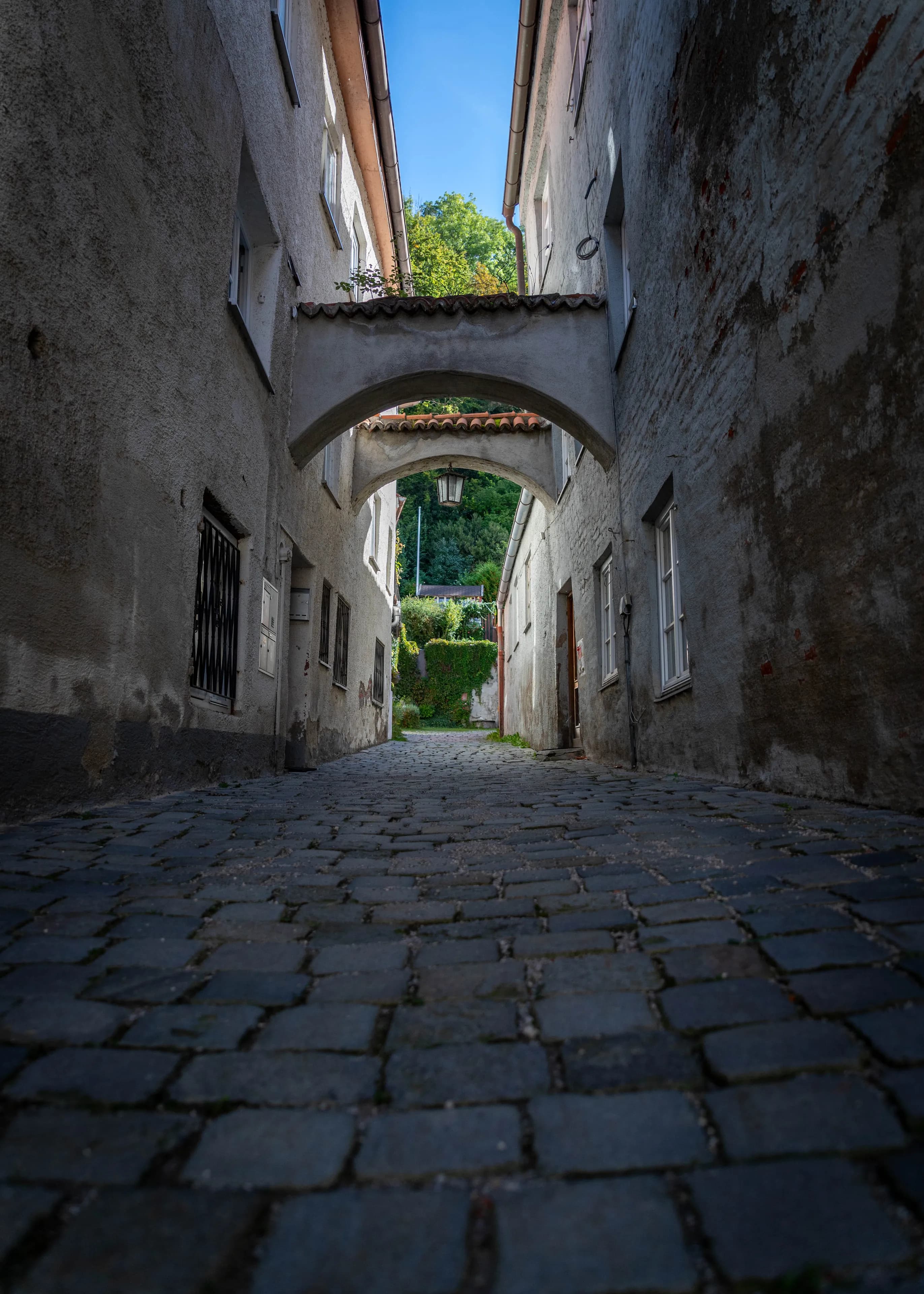 Kopfsteingasse in der Landsberger Altstadt, darüber spannt sich ein Torbogen zwischen zwei Häusern