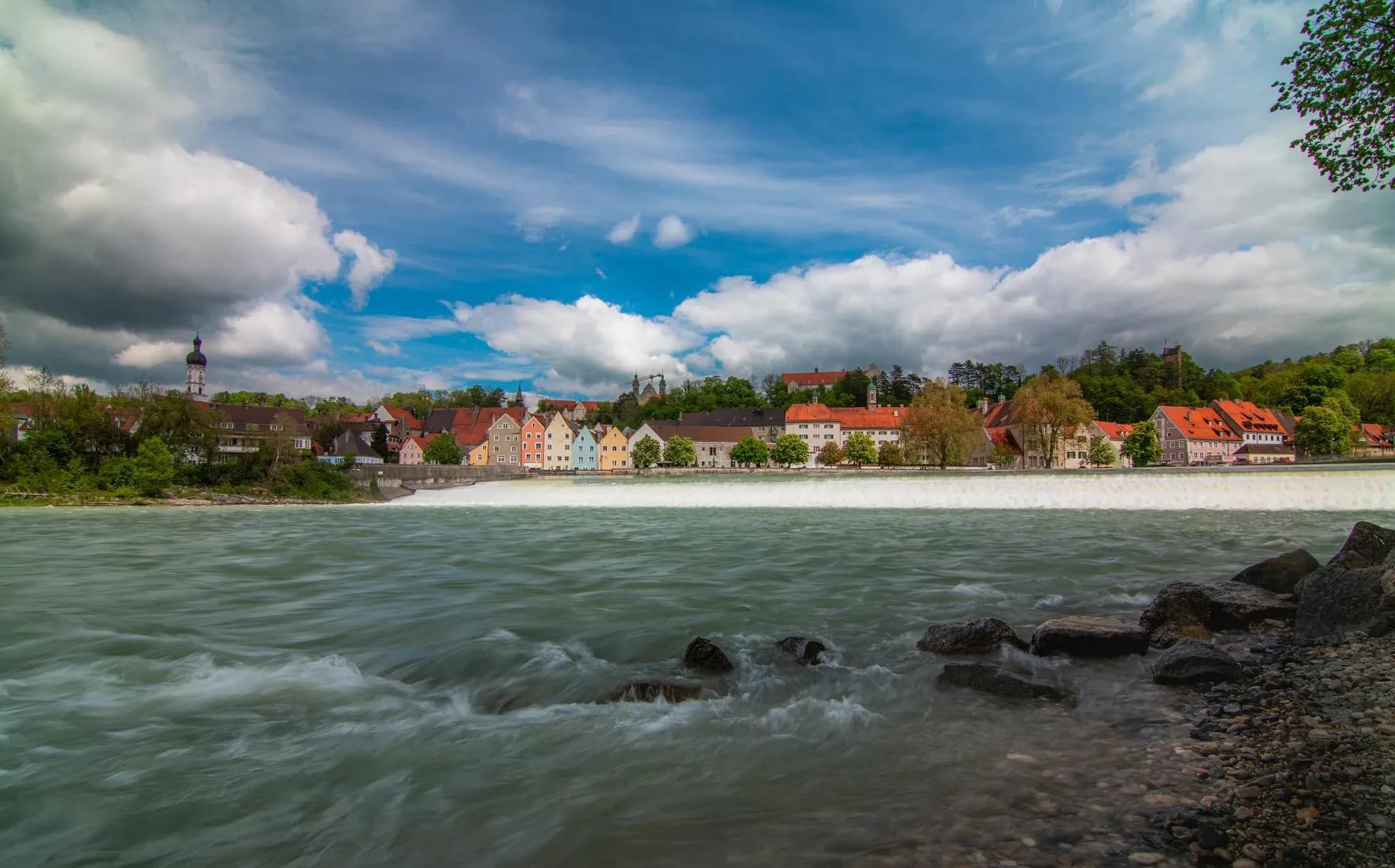 Der Lech strömt über die Steine, dahinter die Häuserzeile von Landsberg