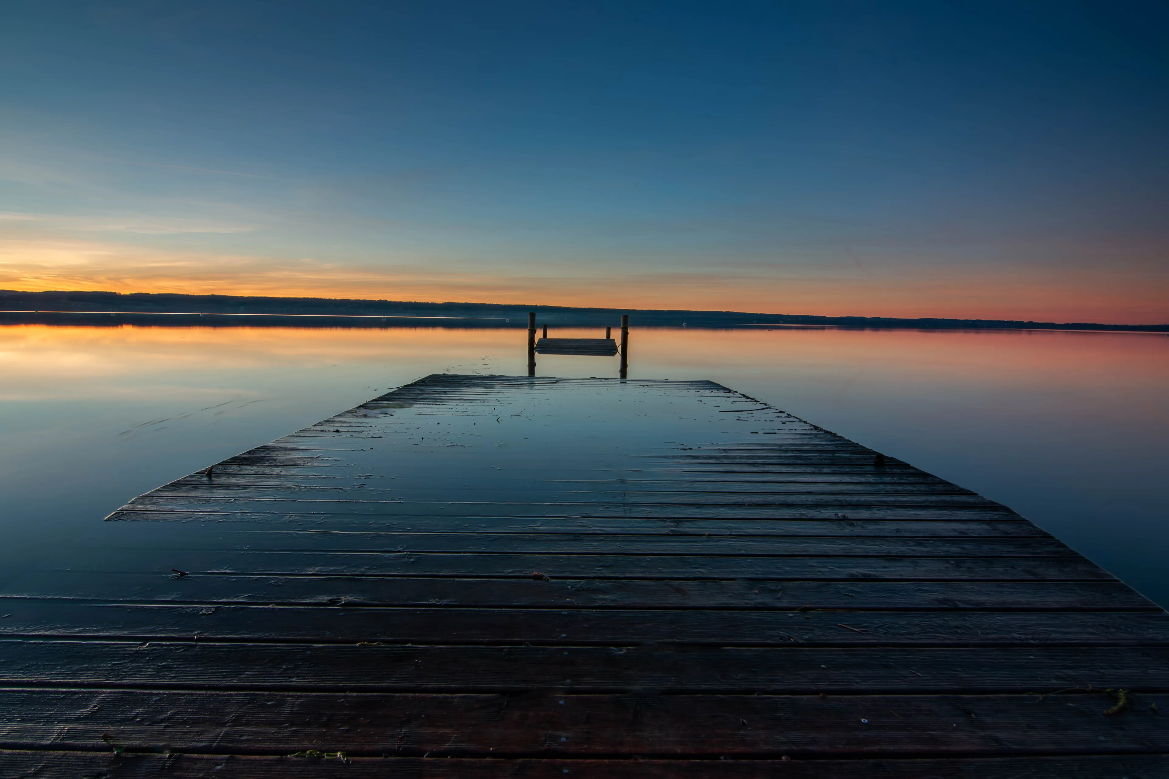 Ein Holzsteg führt in den Ammersee hinaus, dahinter geht die Sonne auf